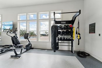 A trx suspension trainer is hanging from the ceiling in a room with a treadmill, exercise bike, and a punching bag.